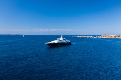During the day under the blue sky, white and black boat sailing on the sea
